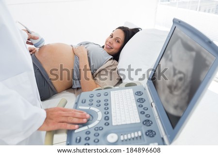 Midsection of male doctor operating ultrasound machine with pregnant woman in background