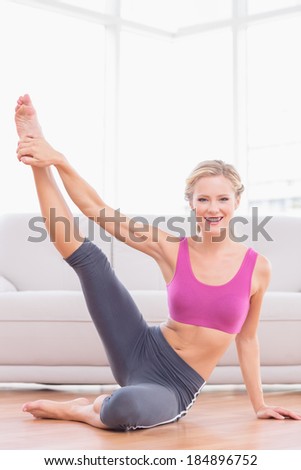 Athletic blonde sitting on floor stretching leg up smiling at camera at home in the living room