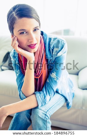 Pretty brunette sitting on sofa smiling at camera at home in the living room