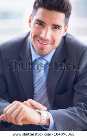Businessman sitting checking his watch smiling at camera in the office
