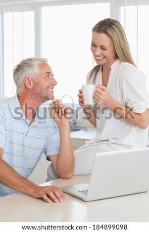 Cheerful couple using laptop together smiling at each other at home in the kitchen