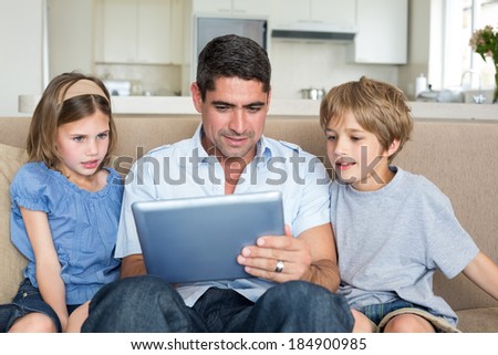 Father teaching to use digital tablet while sitting on sofa at home