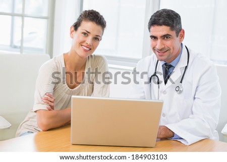 Male doctor and patient using laptop at desk in medical office