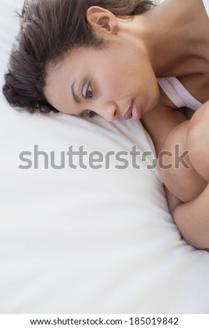 Depressed brunette lying on bed holding her knees at home in the bedroom