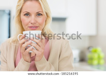 Portrait of a beautiful young woman with coffee cup in the kitchen at home