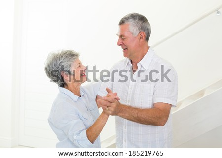 Cheerful senior couple dancing together at home in living room