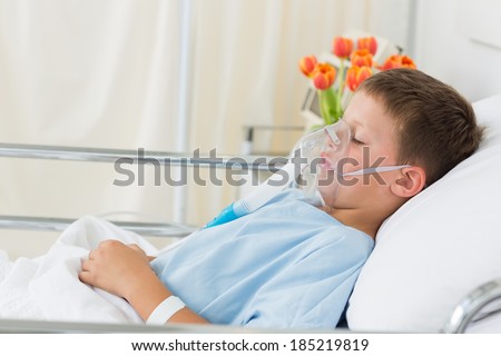 Side view of sick little boy wearing oxygen mask in hospital ward