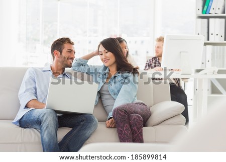 Smiling designers working together on laptop on the couch in creative office