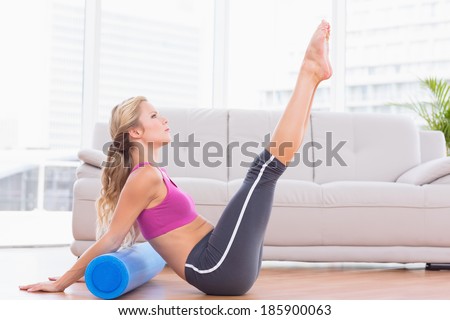 Fit blonde stretching on floor using foam roller at home in the living room