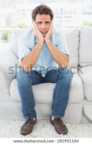 Upset man sitting on the couch looking at camera at home in the living room