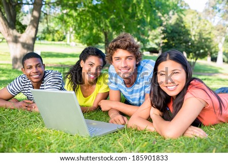 Portrait of university students with laptop lying on grass on college campus