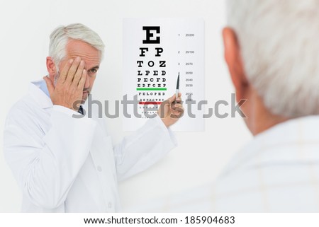 Male pediatrician ophthalmologist with senior patient pointing at eye chart in medical office