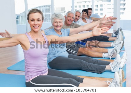 Happy female trainer with class stretching hands at yoga class