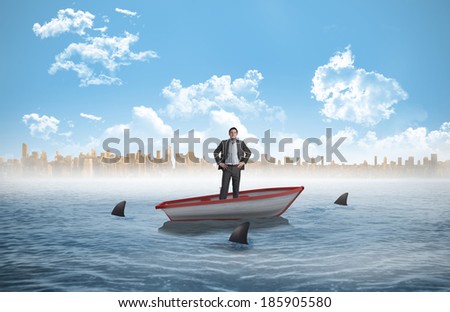 Smiling businessman with hands on hips against sharks circling a small boat in the sea