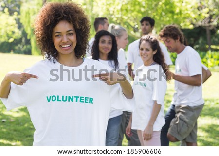 Portrait of happy female volunteer pointing at tshirt with friends in background