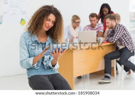 Smiling designer sitting in front of her colleagues using digital tablet in creative office