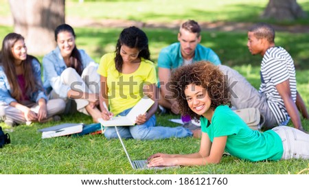 Portrait of happy female student using laptop on campus while friends studying in background