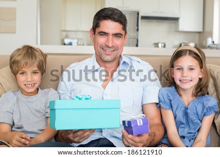 Portrait of father holding gift boxes while sitting with children on sofa at home