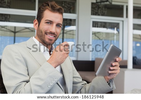 Cheerful young businessman working on tablet drinking espresso in patio of restaurant