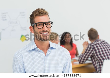Handsome designer smiling at camera with colleagues behind him in creative office