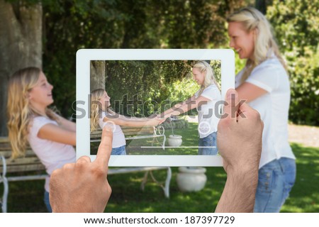 Hand holding tablet pc showing blonde mother and daughter in park