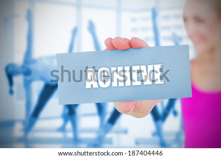 Fit blonde holding card saying achieve against fitness class in gym