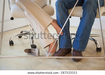 Casual businesswoman playing footsie with colleague under desk in the office