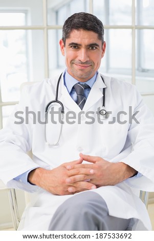 Portrait of a smiling male doctor sitting with hands clasped in the hospital