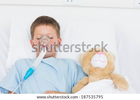Sick boy wearing oxygen mask sleeping beside stuffed toy in hospital bed
