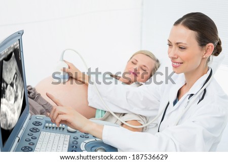 Cheerful female doctor showing woman her baby on ultrasound at the hospital
