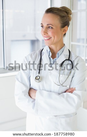 Beautiful happy young female doctor standing with arms crossed in the hospital