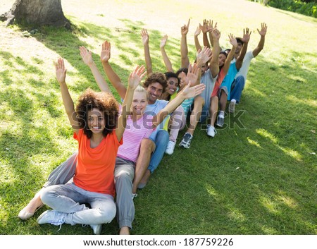 High angle view of excited friends raising hands while sitting on grass in park