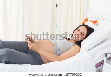 Portrait of happy young pregnant woman lying in bed at hospital
