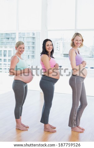 Happy pregnant women standing in a line smiling at camera in a fitness studio