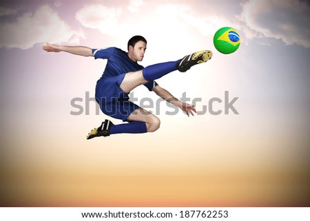 Football player in blue kicking against beautiful orange and blue sky