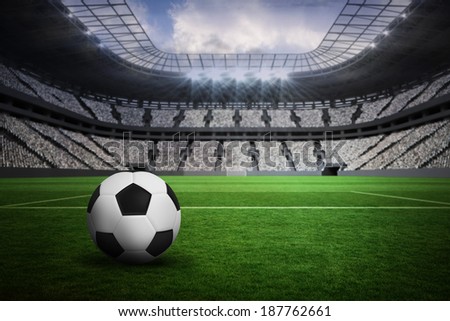 Black and white leather football in a vast football stadium with fans in white