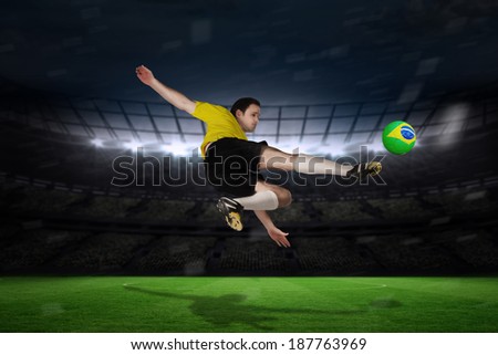 Football player in yellow kicking against large football stadium with fans in yellow