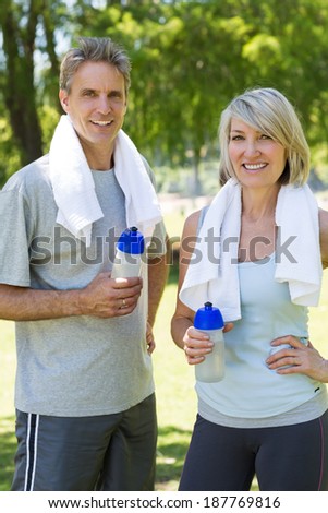 Portrait of happy couple after a workout with towels and water bottles in park