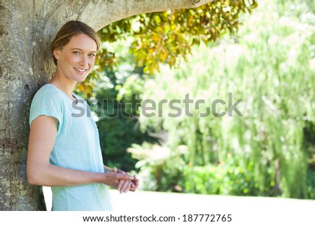 Portrait of a happy young woman leaning against the tree at a park