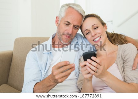 Happy couple sitting on couch texting on their phones at home in the living room