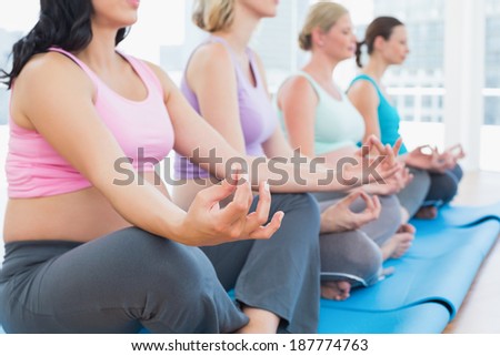 Calm pregnant women meditating in yoga class in a fitness studio