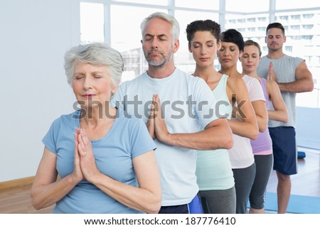 Sporty people with eyes closed and joined hands at a bright fitness studio
