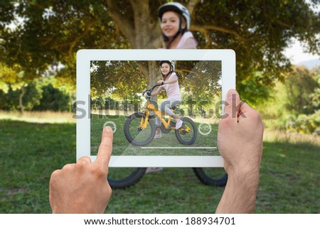 Hand holding tablet pc showing little girl riding her bike in the park