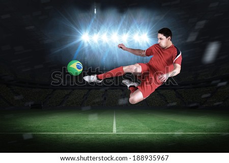Fit football player jumping and kicking in a football pitch under spotlights