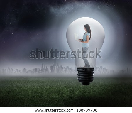 Woman holding laptop in light bulb against city on the horizon