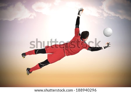 Fit goal keeper jumping up against beautiful orange and blue sky