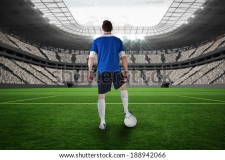 Handsome football player in blue jersey in a vast football stadium with fans in white