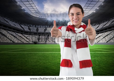 Football fan in white wearing scarf showing thumbs up in a vast football stadium with fans in white