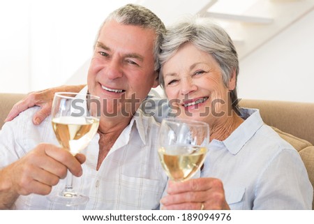 Senior couple sitting on couch having white wine at home in living room