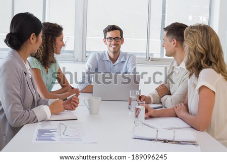 Casual boss smiling at camera dueing meeting with business team in the office